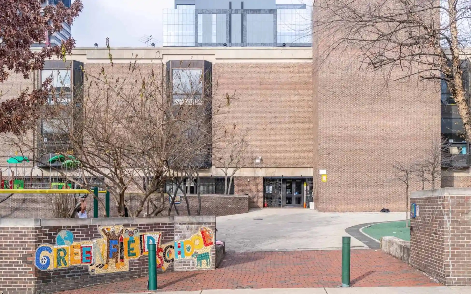 Front entrance and schoolyard of Albert M. Greenfield School in Center City Philadelphia, showing brick building, playground area, and colorful Greenfield mural