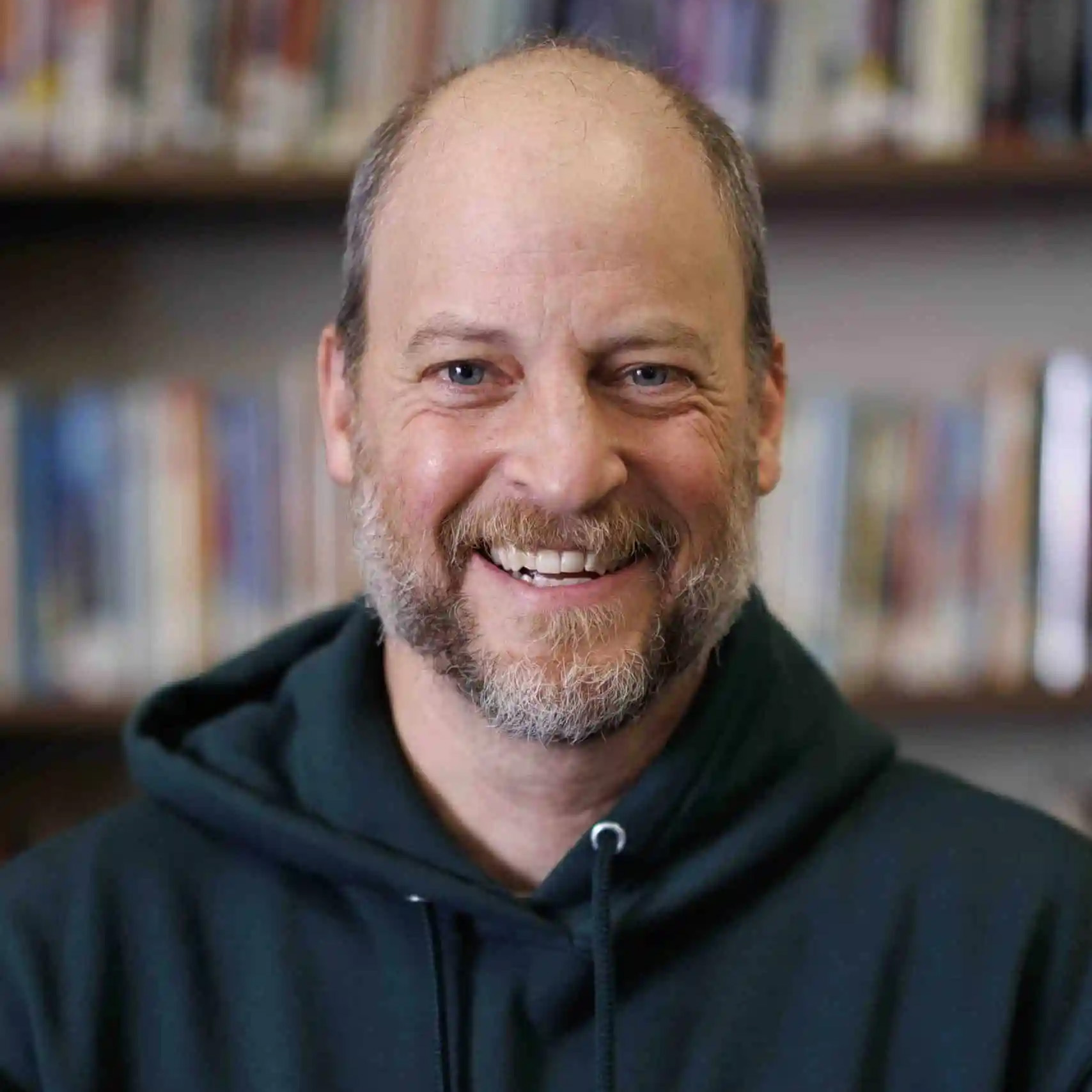 Portrait of Dan Lazar, Principal of Albert M. Greenfield School, smiling in front of a bookshelf